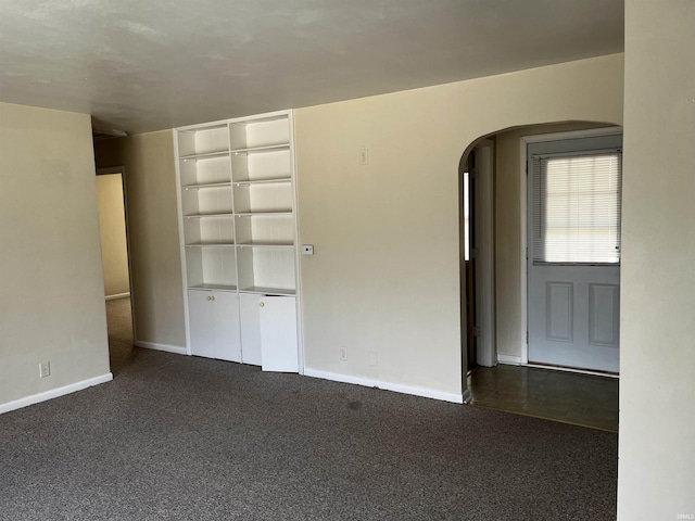 spare room with arched walkways, dark carpet, and baseboards