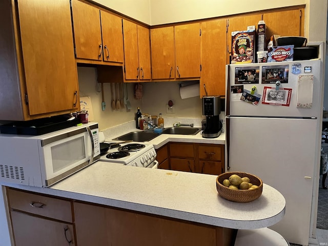 kitchen with a kitchen bar, light countertops, a peninsula, brown cabinetry, and white appliances