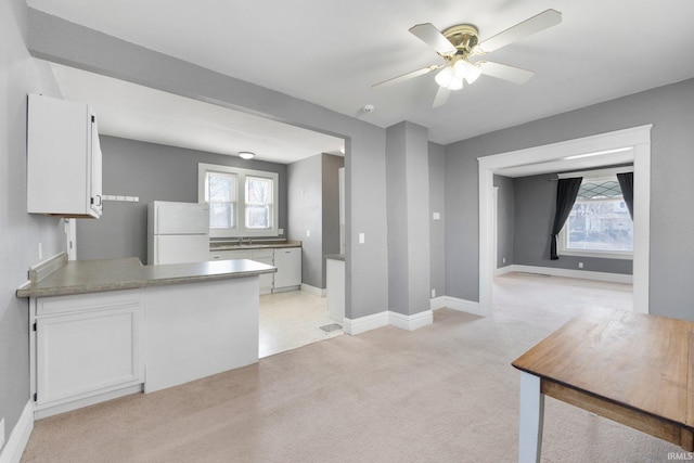 kitchen with light carpet, a sink, white cabinetry, freestanding refrigerator, and a peninsula