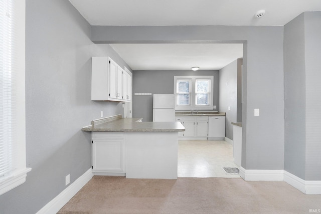 kitchen featuring visible vents, a peninsula, freestanding refrigerator, white cabinetry, and light colored carpet