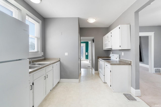 kitchen featuring white appliances, baseboards, visible vents, a sink, and white cabinets