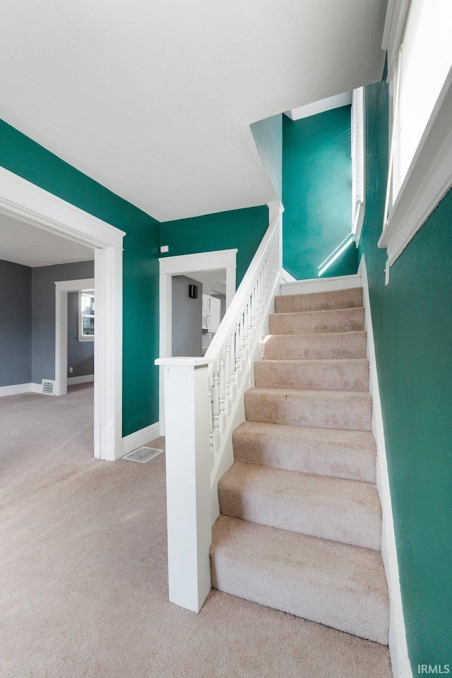 stairway with baseboards, plenty of natural light, and carpet floors