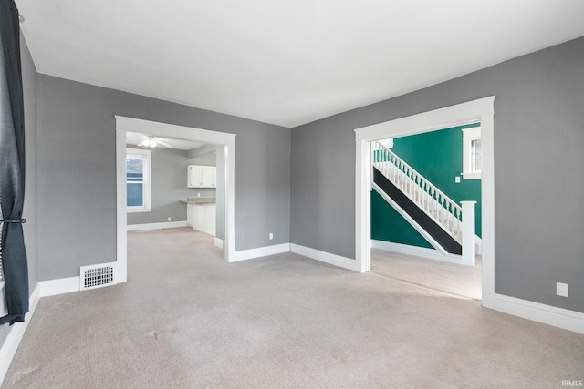 unfurnished living room featuring visible vents, baseboards, carpet, and stairway