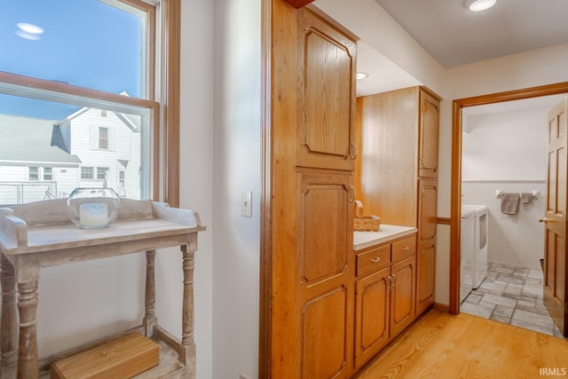 bathroom with a wainscoted wall, wood finished floors, tile walls, vanity, and washing machine and clothes dryer