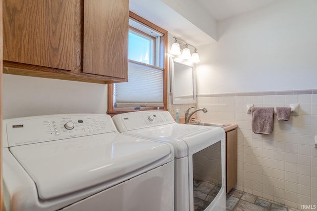 clothes washing area with stone finish flooring, a wainscoted wall, washing machine and dryer, cabinet space, and tile walls