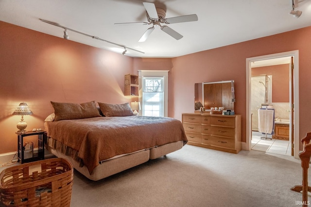 bedroom featuring light carpet, rail lighting, ensuite bath, and a ceiling fan