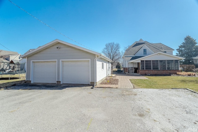 exterior space with a front lawn, a detached garage, a trampoline, an outdoor structure, and brick siding