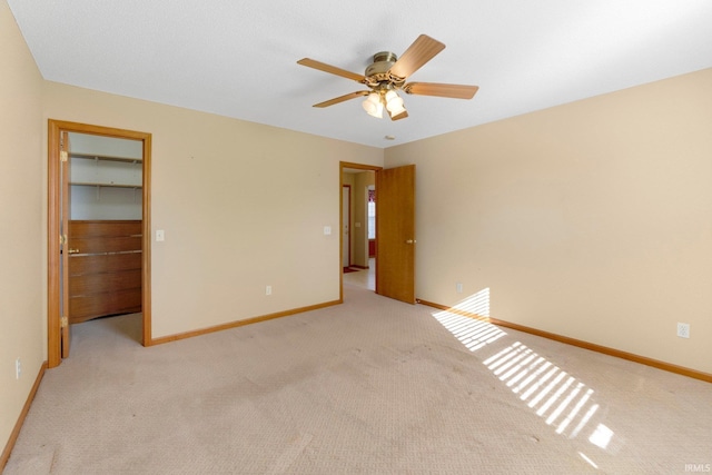 unfurnished bedroom featuring a walk in closet, ceiling fan, baseboards, and light carpet