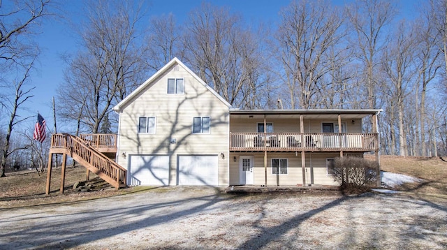 rear view of house featuring stairway, an attached garage, a deck, and driveway