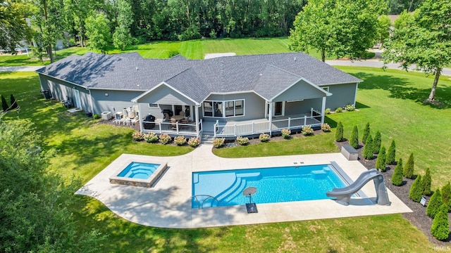 rear view of house with a deck, a yard, a shingled roof, an outdoor pool, and a patio area