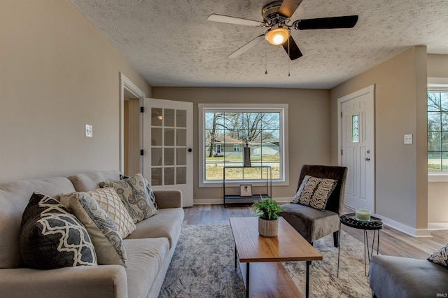 living room featuring baseboards, a textured ceiling, a ceiling fan, and light wood finished floors