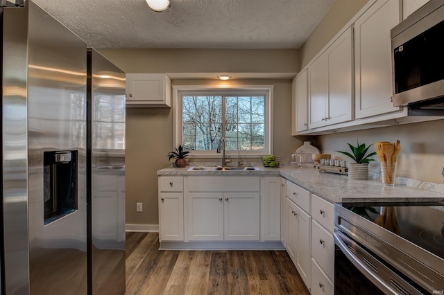 kitchen featuring dark wood-type flooring, appliances with stainless steel finishes, a textured ceiling, white cabinetry, and a sink