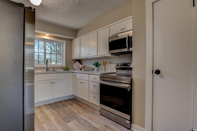 kitchen featuring white cabinetry, light wood finished floors, appliances with stainless steel finishes, and a sink