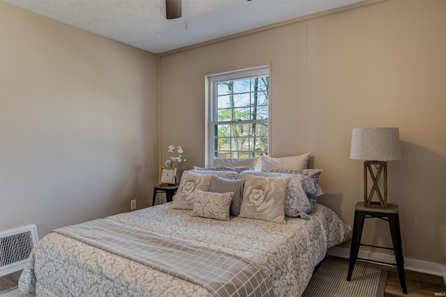 bedroom featuring visible vents, baseboards, wood finished floors, a textured ceiling, and a ceiling fan