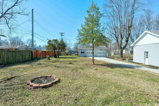 view of yard featuring dirt driveway, a fire pit, a garage, and fence