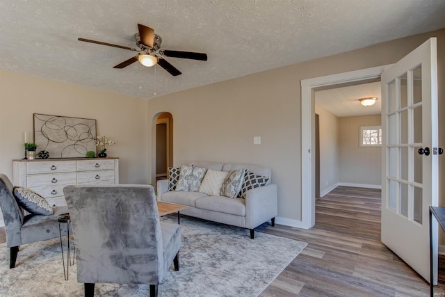 living area with a ceiling fan, a textured ceiling, wood finished floors, arched walkways, and baseboards