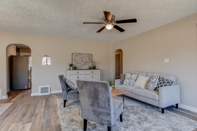 living room featuring arched walkways, visible vents, and light wood-type flooring