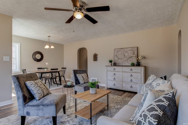 living area with baseboards, wood finished floors, arched walkways, and a textured ceiling