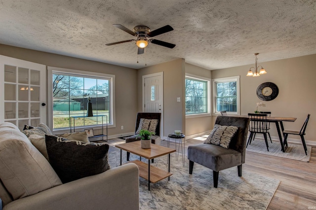 living area featuring light wood finished floors, ceiling fan with notable chandelier, a textured ceiling, and baseboards