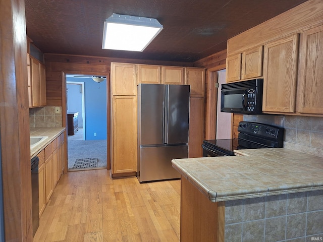 kitchen featuring black appliances, tasteful backsplash, tile countertops, light wood-style floors, and a peninsula