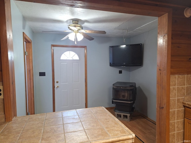 entryway with a ceiling fan, wood finished floors, and a wood stove