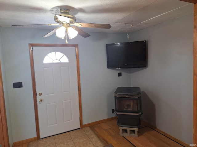 foyer entrance featuring light wood-style flooring, a ceiling fan, a textured ceiling, baseboards, and a wood stove