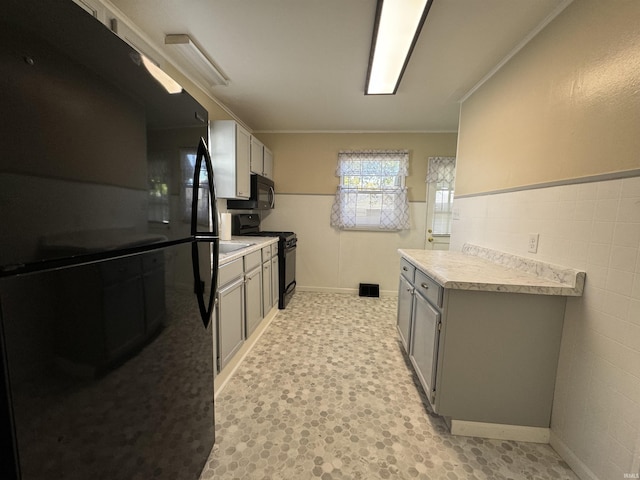 kitchen with gray cabinetry, a wainscoted wall, light floors, light countertops, and black appliances