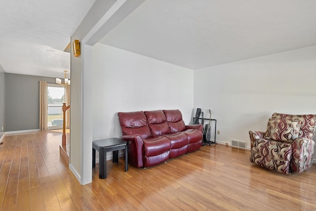 living area featuring visible vents, a textured ceiling, wood finished floors, baseboards, and a chandelier