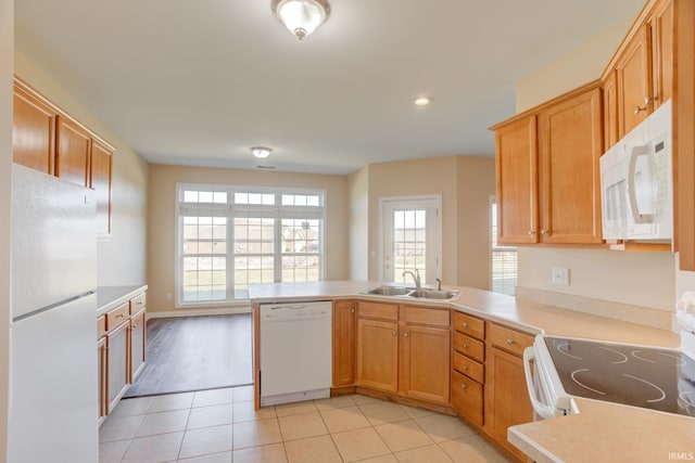 kitchen with a sink, white appliances, a peninsula, light countertops, and light tile patterned floors