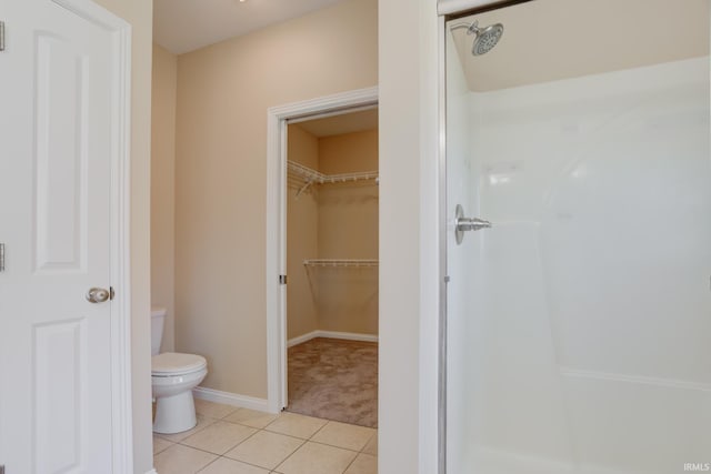 full bath featuring tile patterned floors, a walk in closet, toilet, baseboards, and walk in shower