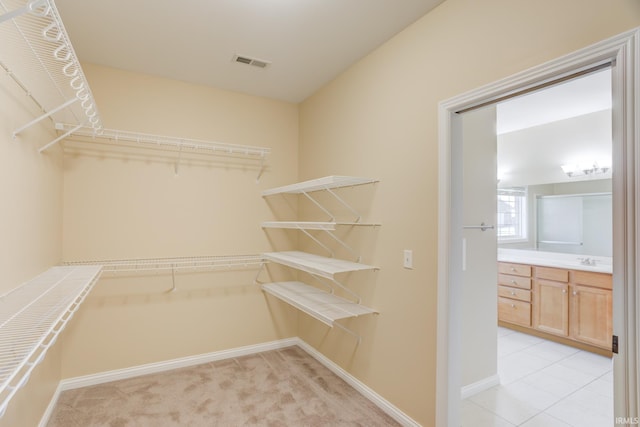 spacious closet with light tile patterned floors, visible vents, light colored carpet, and a sink