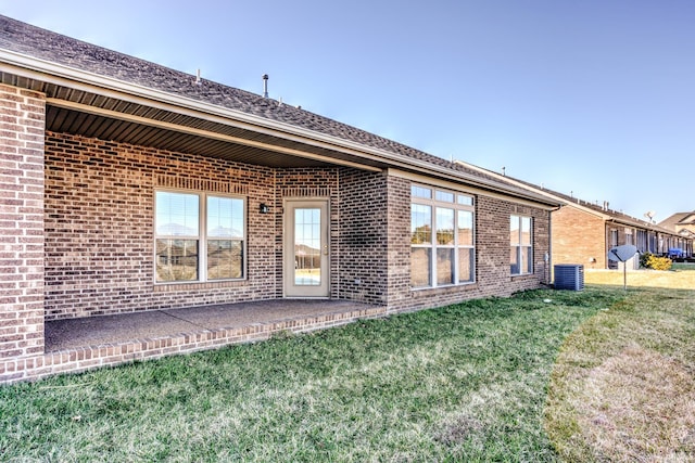 rear view of property with brick siding, central AC unit, a shingled roof, and a yard