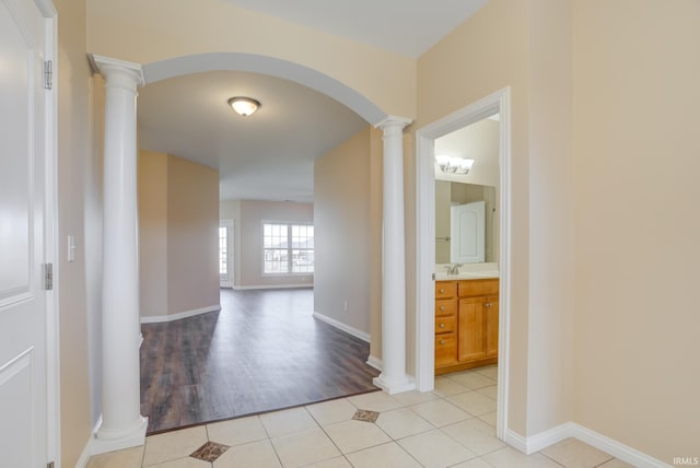 hall featuring light tile patterned floors, decorative columns, arched walkways, and baseboards