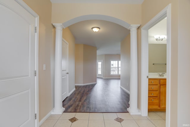 corridor with light tile patterned floors, arched walkways, a sink, and ornate columns