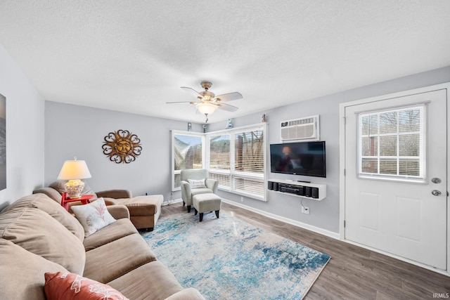 living room with a wall mounted AC, a textured ceiling, wood finished floors, baseboards, and ceiling fan