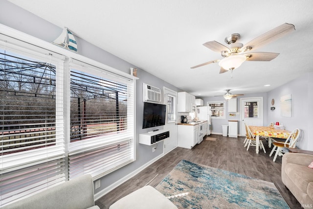 living area featuring a ceiling fan, dark wood-style floors, baseboards, and a wall mounted AC