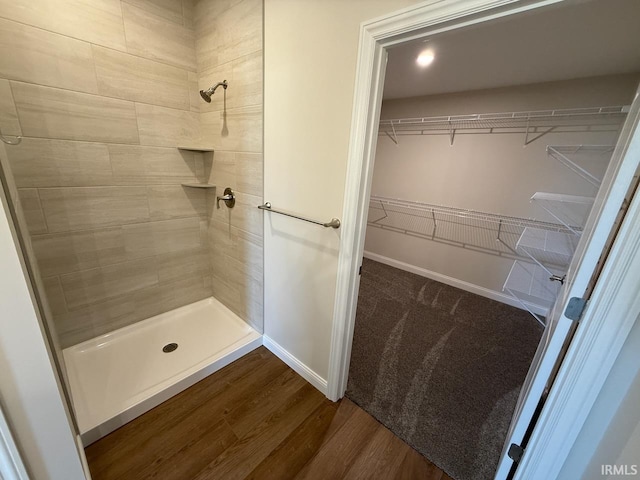 full bath featuring a tile shower, a spacious closet, baseboards, and wood finished floors