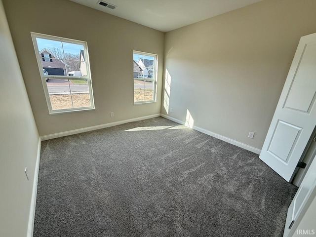 spare room with visible vents, baseboards, and dark colored carpet