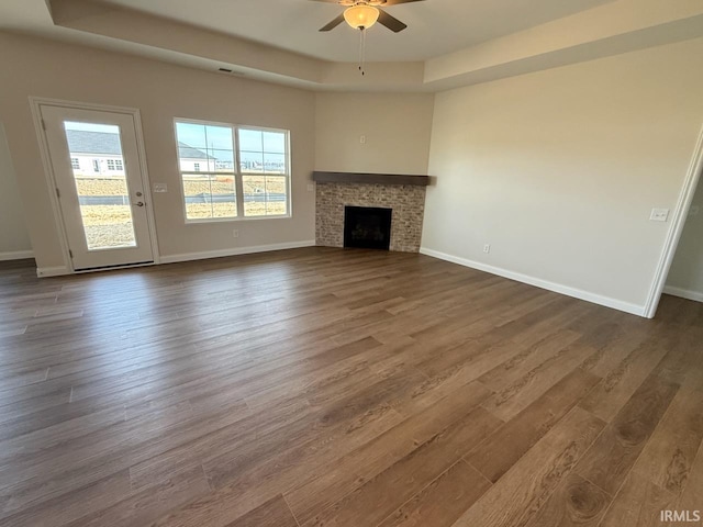 unfurnished living room featuring a raised ceiling, a fireplace, dark wood-type flooring, and baseboards