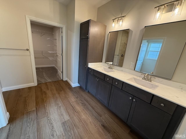 full bathroom with a walk in closet, double vanity, wood finished floors, and a sink