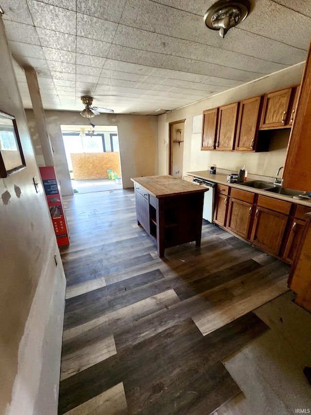 kitchen with dark wood finished floors, dishwashing machine, brown cabinetry, wood counters, and a sink