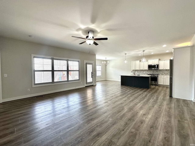 unfurnished living room with dark wood-type flooring, recessed lighting, ceiling fan with notable chandelier, and baseboards