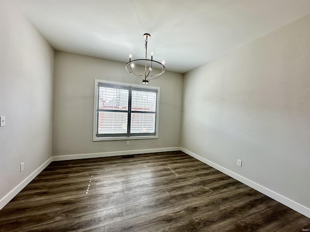 empty room featuring baseboards, an inviting chandelier, and dark wood finished floors