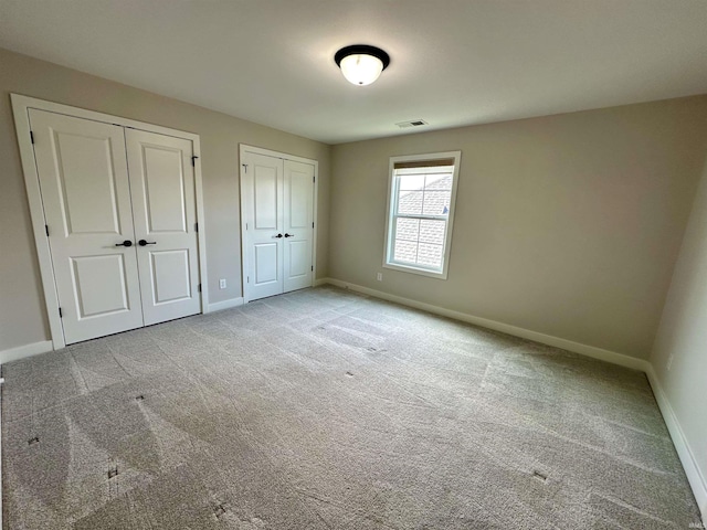 unfurnished bedroom with light carpet, visible vents, two closets, and baseboards