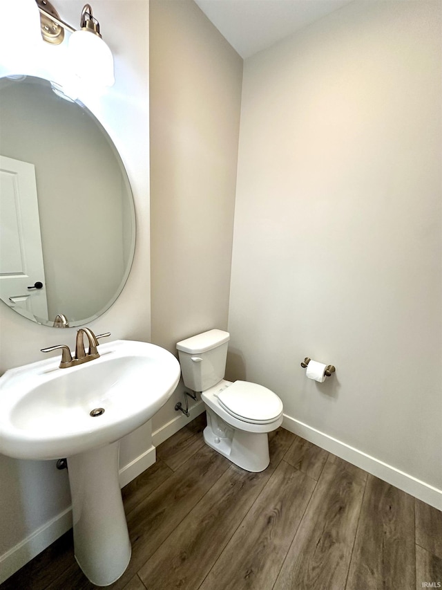 bathroom featuring toilet, wood finished floors, baseboards, and a sink