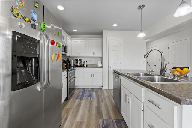 kitchen featuring wood finished floors, a sink, stainless steel appliances, dark countertops, and decorative light fixtures