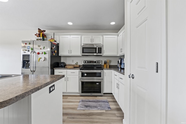 kitchen featuring dark countertops, white cabinets, appliances with stainless steel finishes, and light wood-type flooring