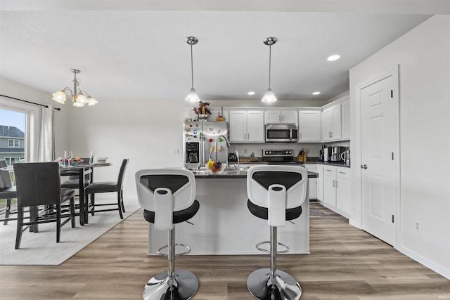 kitchen featuring dark countertops, a breakfast bar area, stainless steel appliances, light wood-style floors, and white cabinetry