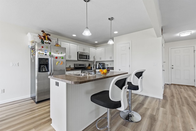 kitchen featuring a breakfast bar, dark countertops, white cabinetry, light wood-style floors, and appliances with stainless steel finishes