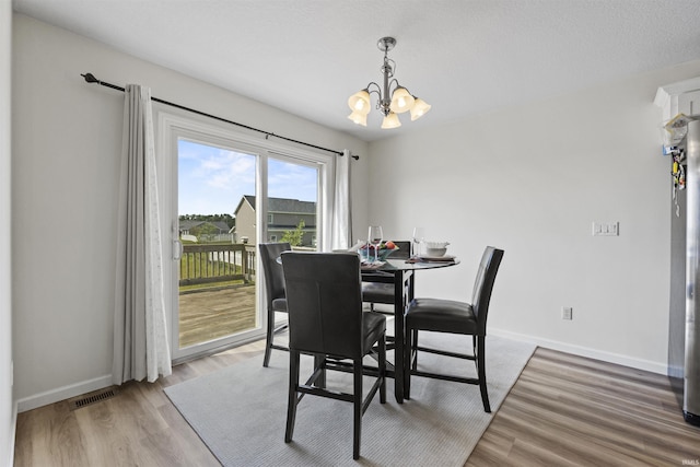 dining area with light wood-style flooring, a notable chandelier, baseboards, and visible vents